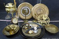 Photo of entire collection showing brassware items and men's watches on brass trays, including incense burner, etched plates, candle holders, bowls, and watches with various bands and faces.