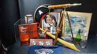 Overview of lot showing telescope on tripod, pirate hat, framed artworks, cutlass, oar, decanters, tins, book and display items
