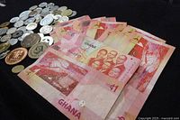 Eight Ghana 1 Cedi banknotes fanned out with assorted world coins