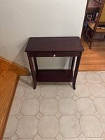Wooden console table positioned near stairs showing front view on tiled floor.
