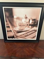 Front view of the black framed black and white photo featuring a coffee cup with 'Cafe De Flore' and a newspaper with 'Firenze' on the wooden counter.