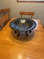 Black and white ceramic plate with botanical leaf pattern on a black iron stand displayed on wooden table with carved wooden chairs in background