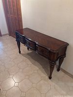 View of wooden console table with curved front and three drawers along a hallway wall.