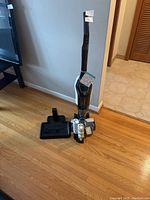 Full view of Bissell Crosswave cleaner with base and accessories on wood floor near wall and door