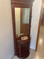 Full view of the tall wooden hallway mirror with rectangular glass panel, decorative top molding, four brass coat hooks on the sides, and semi-circular shelf at the bottom with turned legs and a bottom shelf.