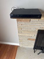 Front view showing the glossy black front panel with control knob on right side, disc tray closed.