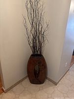 Photo showing tall handmade ceramic vase with oval cut-out, placed in corner with dried branches inside.