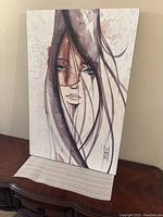 Front view of the modern art wooden framed picture showing the stylized portrait of a woman with long hair and artist signature.