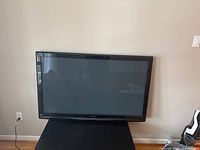 Front view of Panasonic 50 inch TV on a black stand in a room with hardwood floor and beige walls.