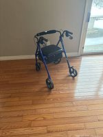 Blue portable folding rollator walker with 4 wheels, padded seat and black storage bag beneath seat, photo taken from front-left angle.