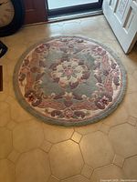 Round decorative entrance floor rug laid on beige tiled floor near door, showing overall pattern and condition.