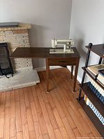Sewing machine mounted in wooden cabinet with drawer and fold-out extension, showing full cabinet and machine setup