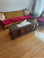 Photo of the solid wood vintage coffee table positioned in front of a vintage sofa and armchair, showing the table top and front doors.