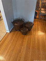 Three decorative metal baskets arranged by size against a wall on a wooden floor.