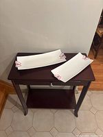 Two white rectangular serving trays with pink butterfly accents on corners placed on a small wooden table