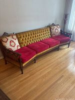 Photo of the vintage couch showing the mustard yellow button-tufted backrest, red velvet seat cushions, and wooden carved armchair frame with decorative pillows.