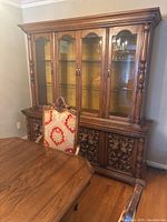 Full view of wooden hutch against wall, showing upper glass doors, lower carved panels, and part of a dining table and chair in front.