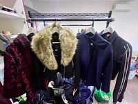 Photo showing five jackets hanging on rack including black coat with faux fur collar, burgundy floral jacket, navy and black jackets
