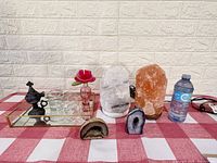 Full view of all items on the checkered cloth: rectangular mirror tray with black ornate container, clear candle holder, pink flower perfume bottle; two tall crystal lamps (white and orange-pink Himalayan salt lamp); two crystal geode pieces (brown polished and blue amethyst standing geode).