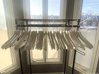 47 white wooden hangers hanging on a black metal rack in front of a large window. The hangers are stained and show signs of use.