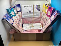 Box with incense sticks arranged in a semi-circle with incense tray, holder stick, and amethyst crystal necklace with card inside.