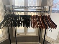 Clothing rack with 67 hangers including 22 wooden hangers on the right side and 45 black suede hangers on the left side, displayed in front of a window with natural light.