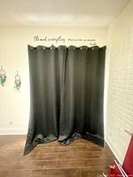 Photo of two black blackout curtains hanging side by side, covering the window, showing their length and grommet tops.