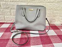 Front view showing grey purse with handles and gold-tone Kate Spade logo plaque