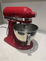 Front-left view of red stand mixer with bowl and whisk attached