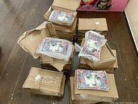Stacks of cardboard boxes containing multiple mini ceramic plates with a face surrounded by colorful floral designs.