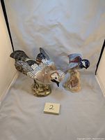 Two ceramic bird statues on cloth backdrop, showing relative size and shape