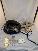 View of a large quantity of silver-toned coins spilling from a small black zippered pouch. Coins feature embossed images and text related to NHL players, mostly Alexander Mogilny.