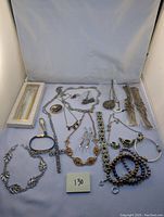 Full view of the mixed jewelry lot spread on a surface showing various metallic chains, bracelets and pendants including a boxed set with two items and some loose pieces.