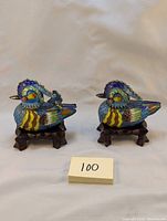 Front view of both cloisonne enamel duck shakers on wooden stands with identification card visible.