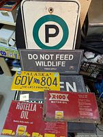 Front view of lot showing Alaska license plate, various policy and parking metal signs, and two flattened Shell motor oil canisters.