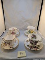Four vintage fine bone china teacups and matching saucers displayed together, showing various floral patterns and gold trim details.