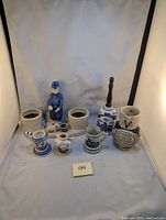 Front view of all ceramic items including candle holder, Dutch boy planter, stein, creamer, bell, and jug on light backdrop.