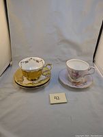 Two Paragon teacups with three saucers displayed, one yellow and gold decorated set, one pink rose patterned set, and one green saucer without a cup.