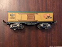 Side view of vintage Lionel Trains boxcar model 1679 with Baby Ruth branding, showing yellow painted metal body, brown sliding door, and black wheels.