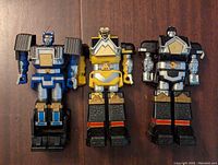 Front view of three assembled Power Rangers Shogun Megazord Zords in blue, yellow, and black colors on wooden surface.