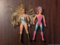 Front view of She-Ra and Glimmer action figures standing side by side on a dark wooden surface.
