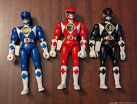 Photo showing the three Power Rangers figures (Blue, Red, Black) standing side-by-side on a wood surface.