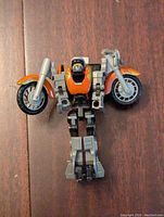 Front view of Transformers Robots in Disguise Lugnutz action figure in robot mode showing orange, black, and gray colors with visible motorcycle wheels.