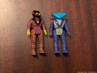 Front view of two Dino Riders figures on a wood surface, showcasing the brown and purple figures.