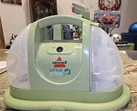 Front view of the Bissell Little Green portable carpet and upholstery cleaner showing power switch, brand logo, two transparent water tanks, and handle.