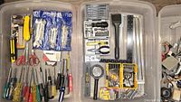 Photo of assorted screwdrivers, scissors, pack of wrenches in blue packaging, utility knives with yellow handles, architectural rulers, pliers, and screwdriver bit sets.