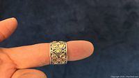Ring worn on finger showing front face with gold heart decoration against silver background.