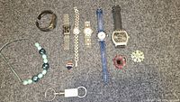 Overview photo showing all watches, bracelets, brooches, jewelry box and keychain in the lot.
