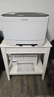 Photo showing Lexmark CS417dn color laser printer on a white shelf with black control panel on top