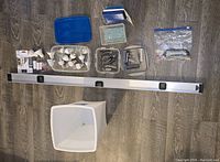 Tools and hardware arranged on floor including the 4-foot level, screw bits, sandpaper, wire tie-downs, and bucket